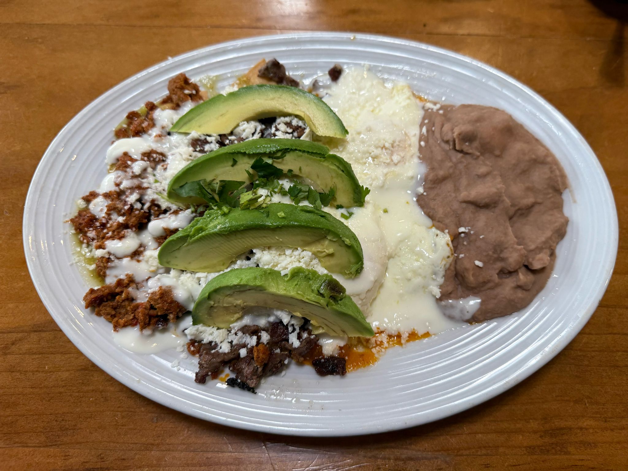 Charlie Chilaquiles!! New Breakfast plate, fried tortilla chips covered with green sauce, ranchero sauce, mexican crema, queso fresco, two eggs any style, served with chorizo , asada meat, avocado slices and refried beans
